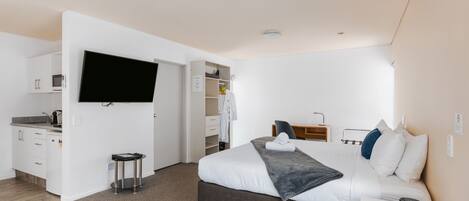 A modern hotel room with a large bed, a flat-screen TV mounted on the wall, a small kitchenette, and a walk-in closet.