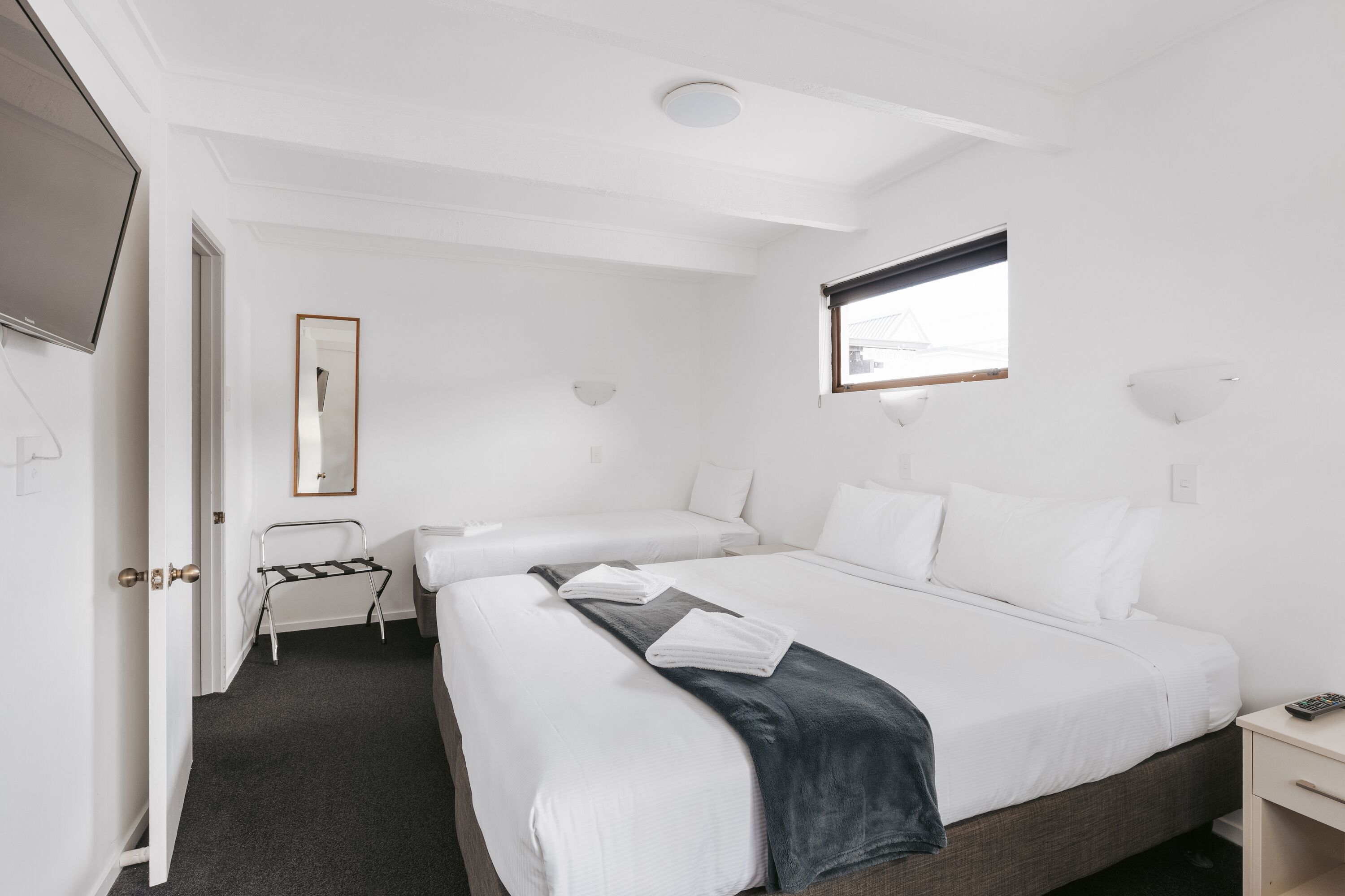 A hotel room with two beds, a TV, a window, and a door.