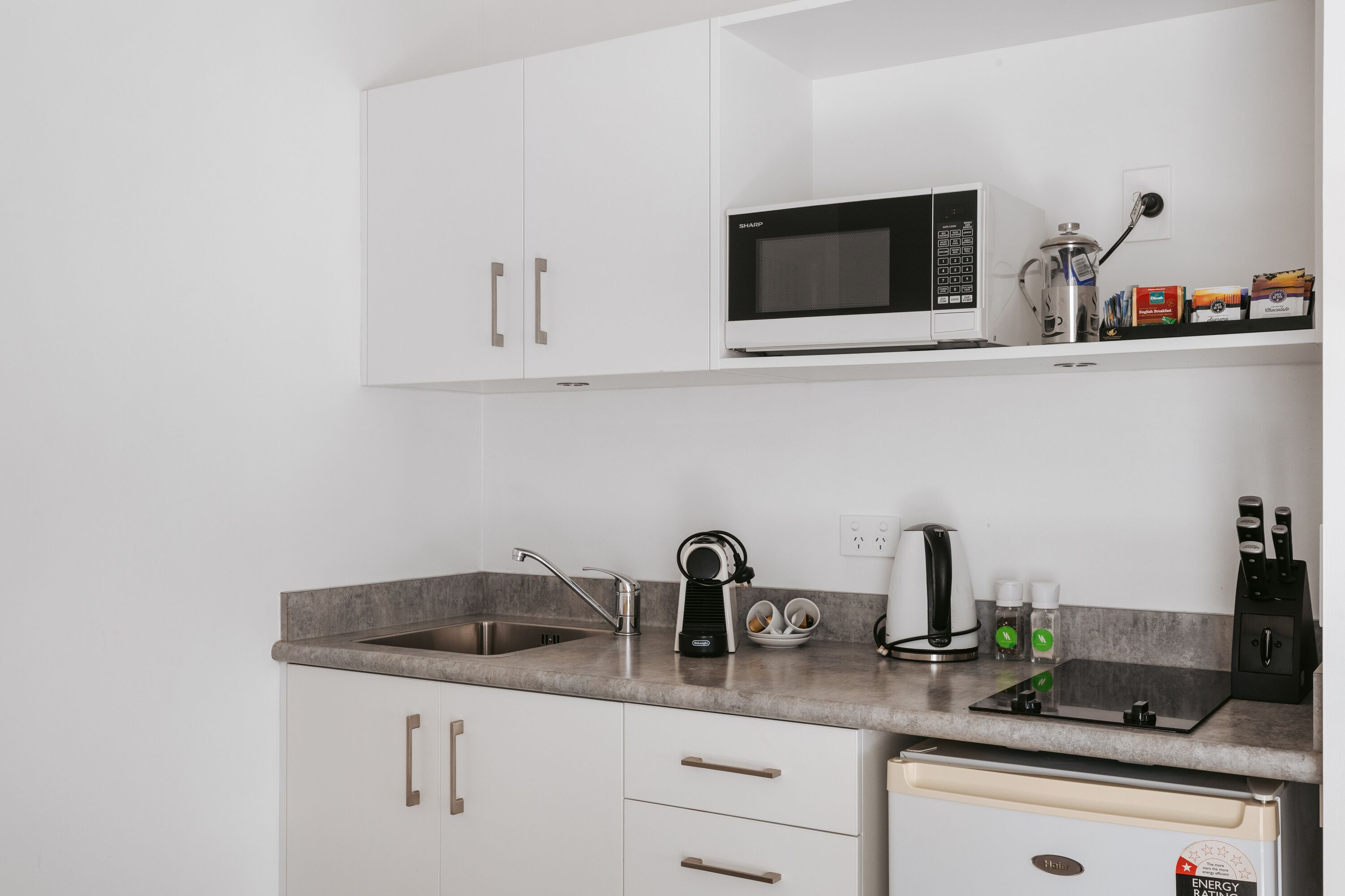 A modern kitchen with white cabinets, a built-in microwave, a coffee maker, and a kettle.