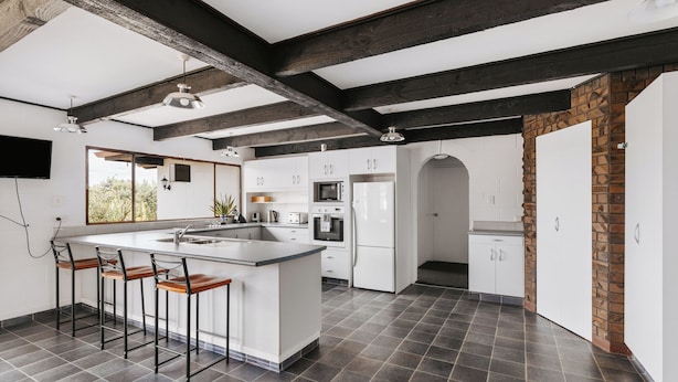 A modern kitchen with a large island, bar stools, and a stone accent wall. - Rolleston Motel Thames – Wenzel Motels (Thames)