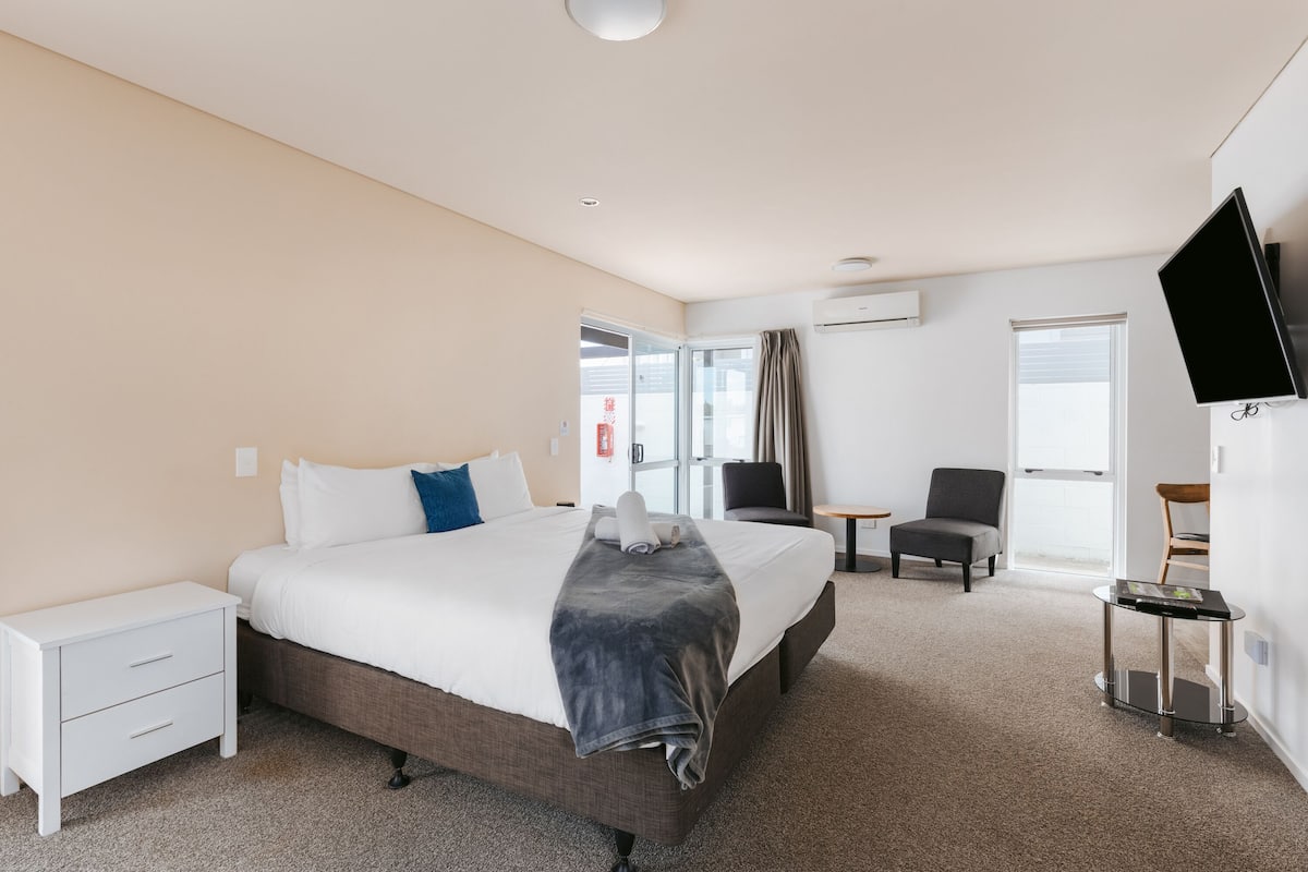 A hotel room with a bed, a desk, a chair, a TV, and a window.