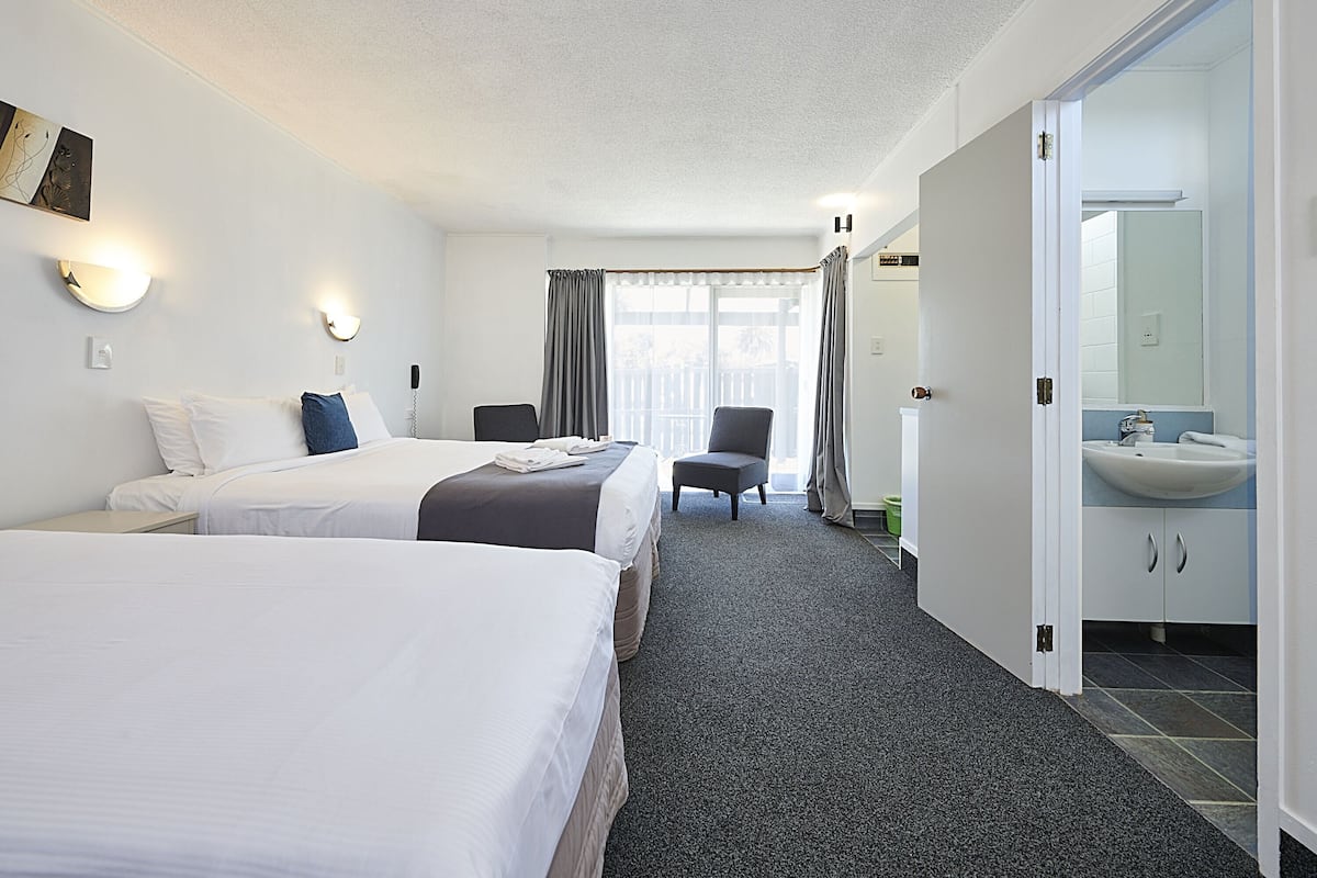 A hotel room with two beds, a sitting area, a bathroom with a sink and mirror, and a view of the outdoors.