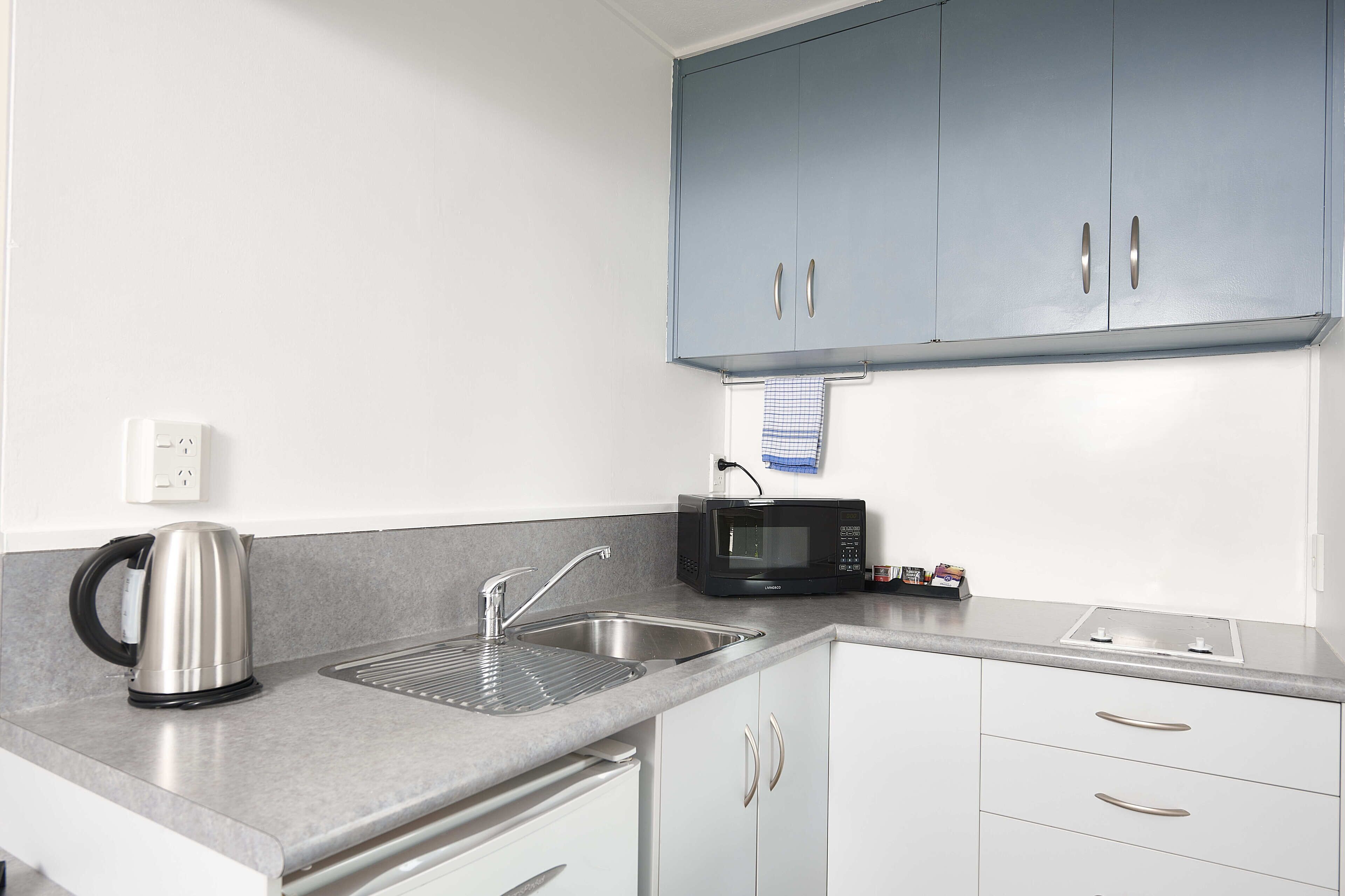 A modern kitchen with a kettle, sink, microwave, and cabinets.