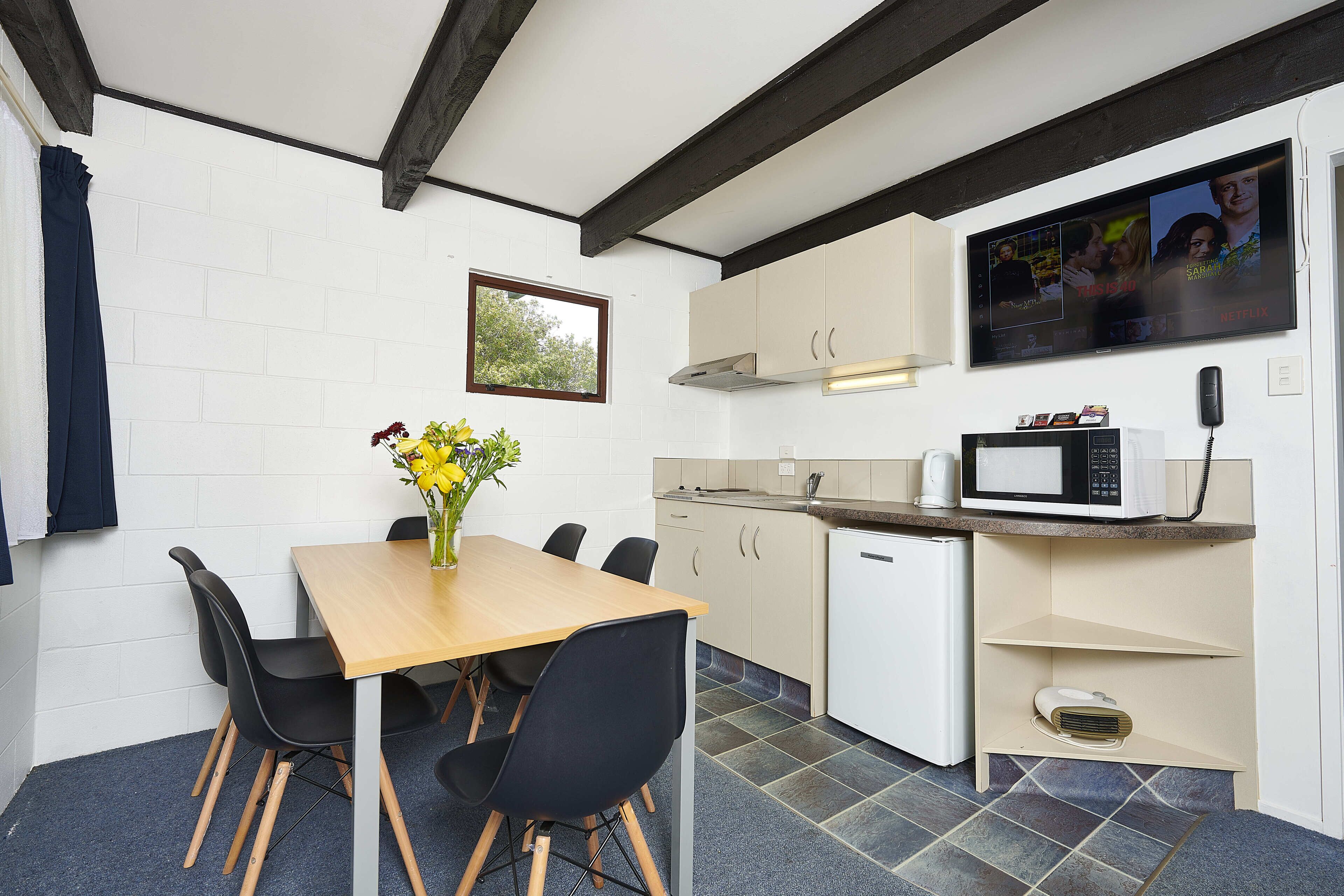 A compact kitchen with a wooden table, black chairs, a microwave, and a small refrigerator.