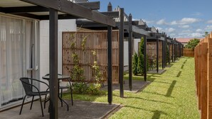 A row of wooden structures with attached tables and chairs, a grassy area, and a clear sky. - Rolleston Motel Thames – Wenzel Motels (Thames)