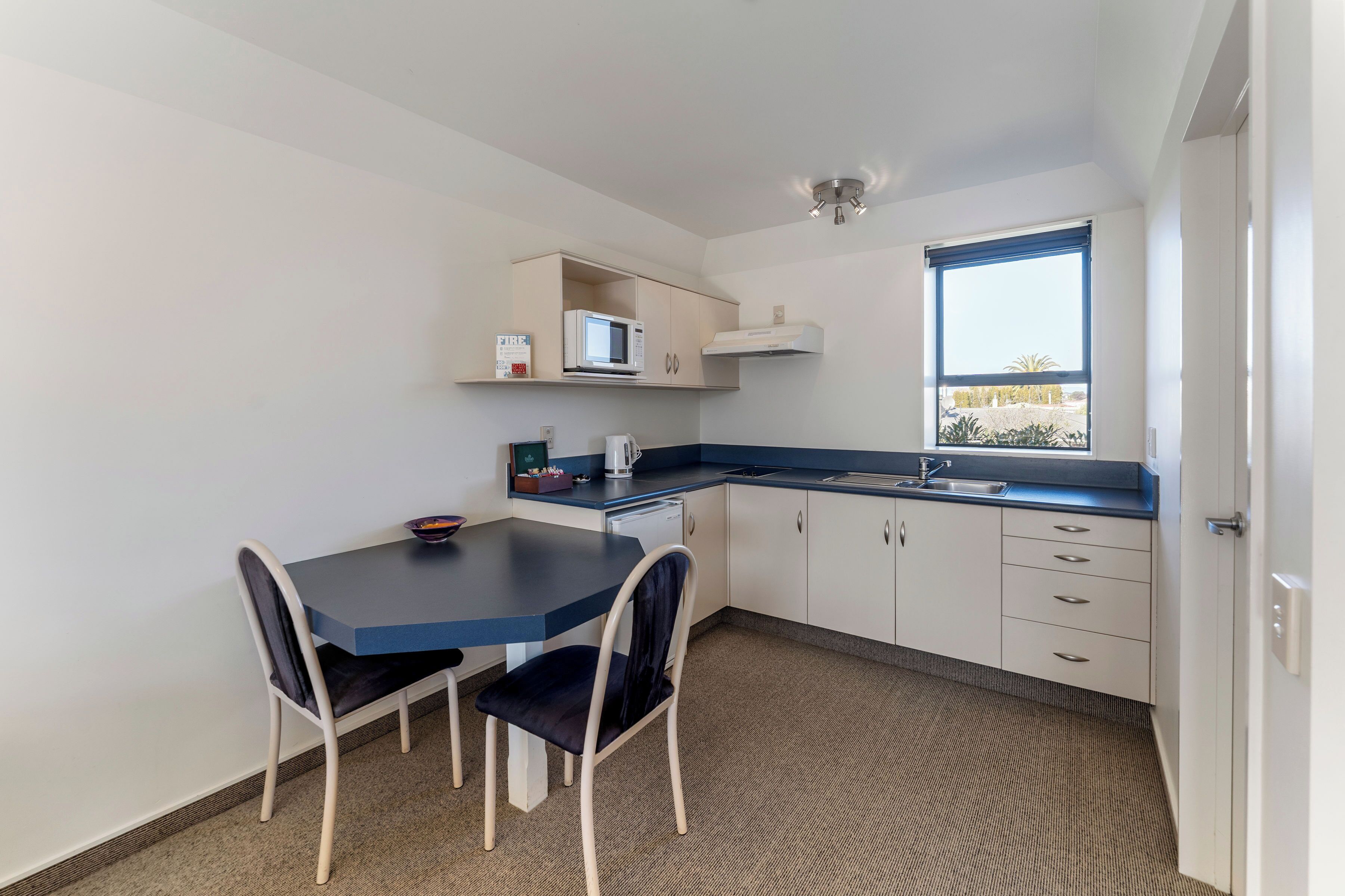 A compact kitchen with a blue countertop, white cabinets, a microwave, and a window with a view.