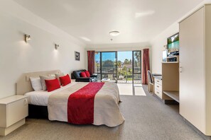 A modern hotel room with a large bed, a desk, and a balcony with a view. - Avalon Manor Motel (Motueka)