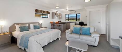 A modern hotel room with a bed, a sofa, a small table, and a kitchenette.
