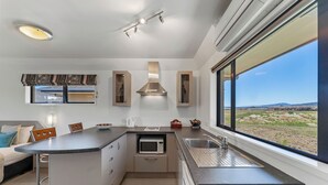 A modern kitchen with a central island, built-in microwave, and a large window offering a view of the landscape. - Avalon Manor Motel (Motueka)