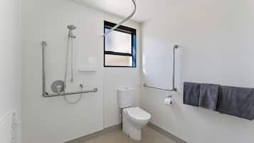 Un baño con inodoro, barras de apoyo, ducha y ventana.