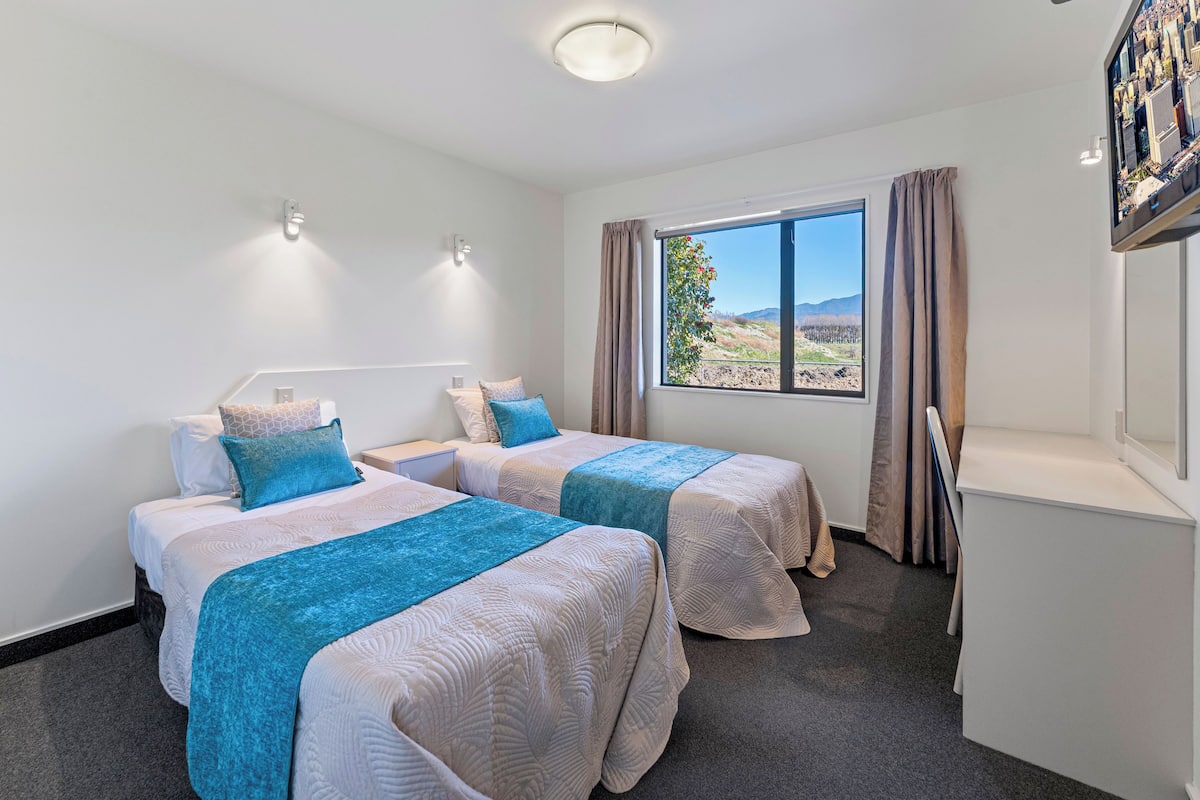 A hotel room with two beds, a desk, and a large window offering a view of the outdoors.