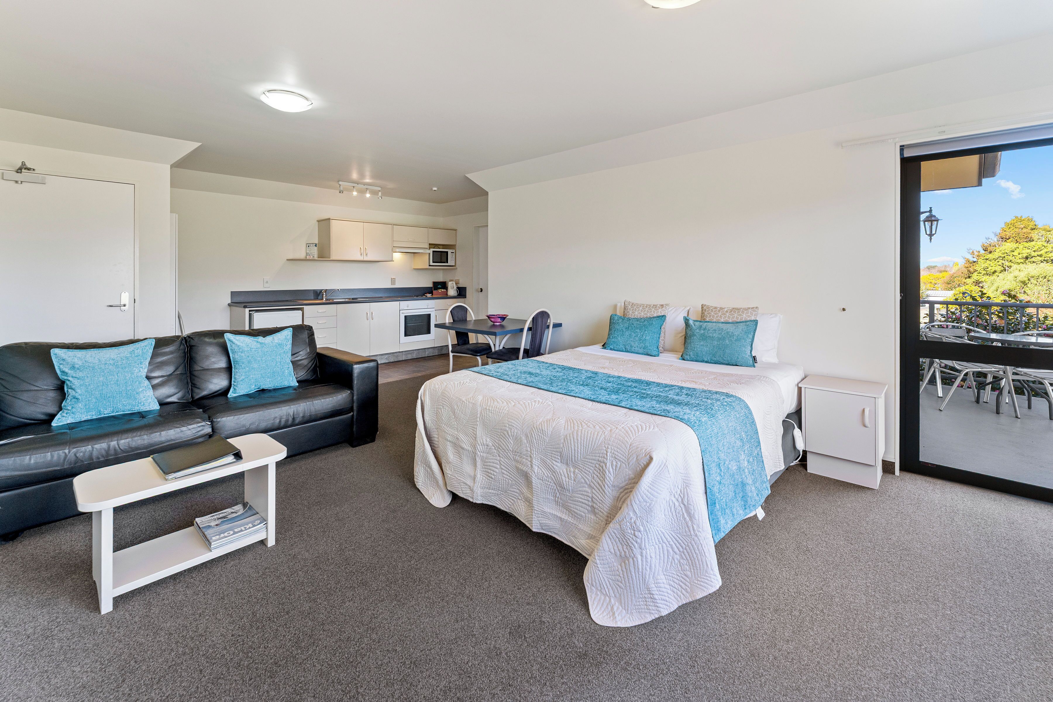 A modern room with a bed, a sofa, a small table, a kitchenette, and a balcony with a view.