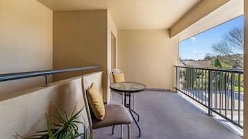 A balcony with a chair and table, beige walls, and a view of a parking lot and buildings.