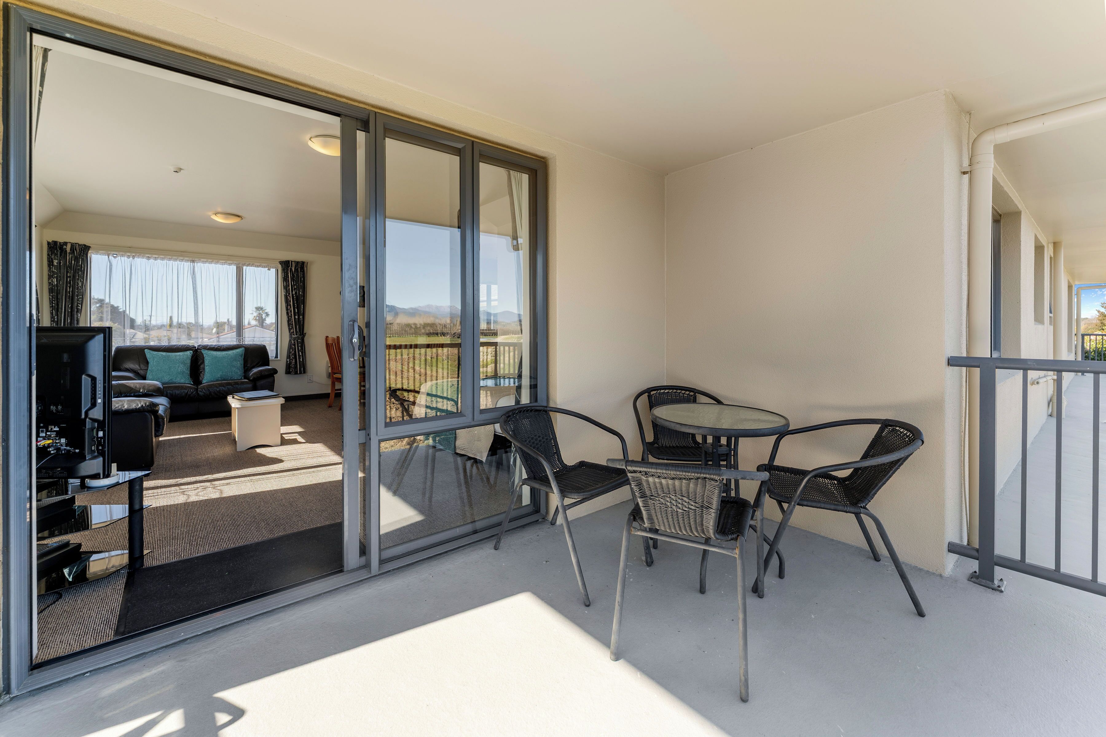 A balcony with a glass door leading to a living area, furnished with a sofa, TV, and a table with chairs.