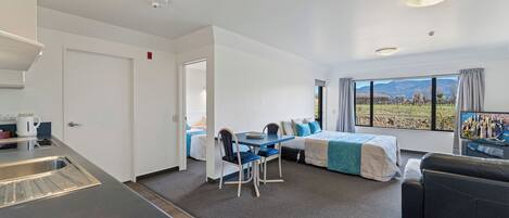 Una habitación de hotel moderna con kitchenette, zona de comedor, cama con vistas y sofá.