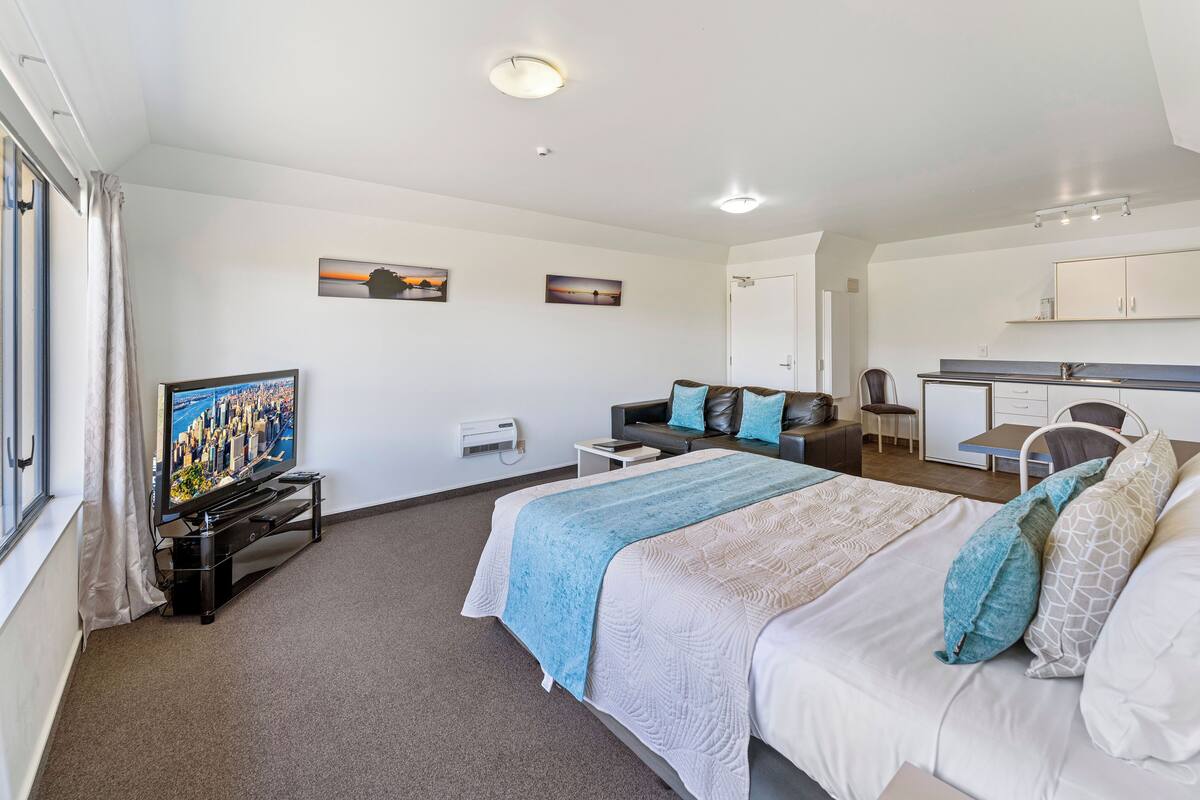 A hotel room with a bed, a TV, a desk, and a kitchenette.