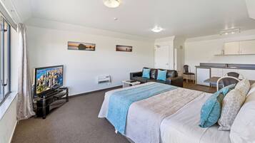 A hotel room with a bed, a TV, a desk, and a kitchenette.