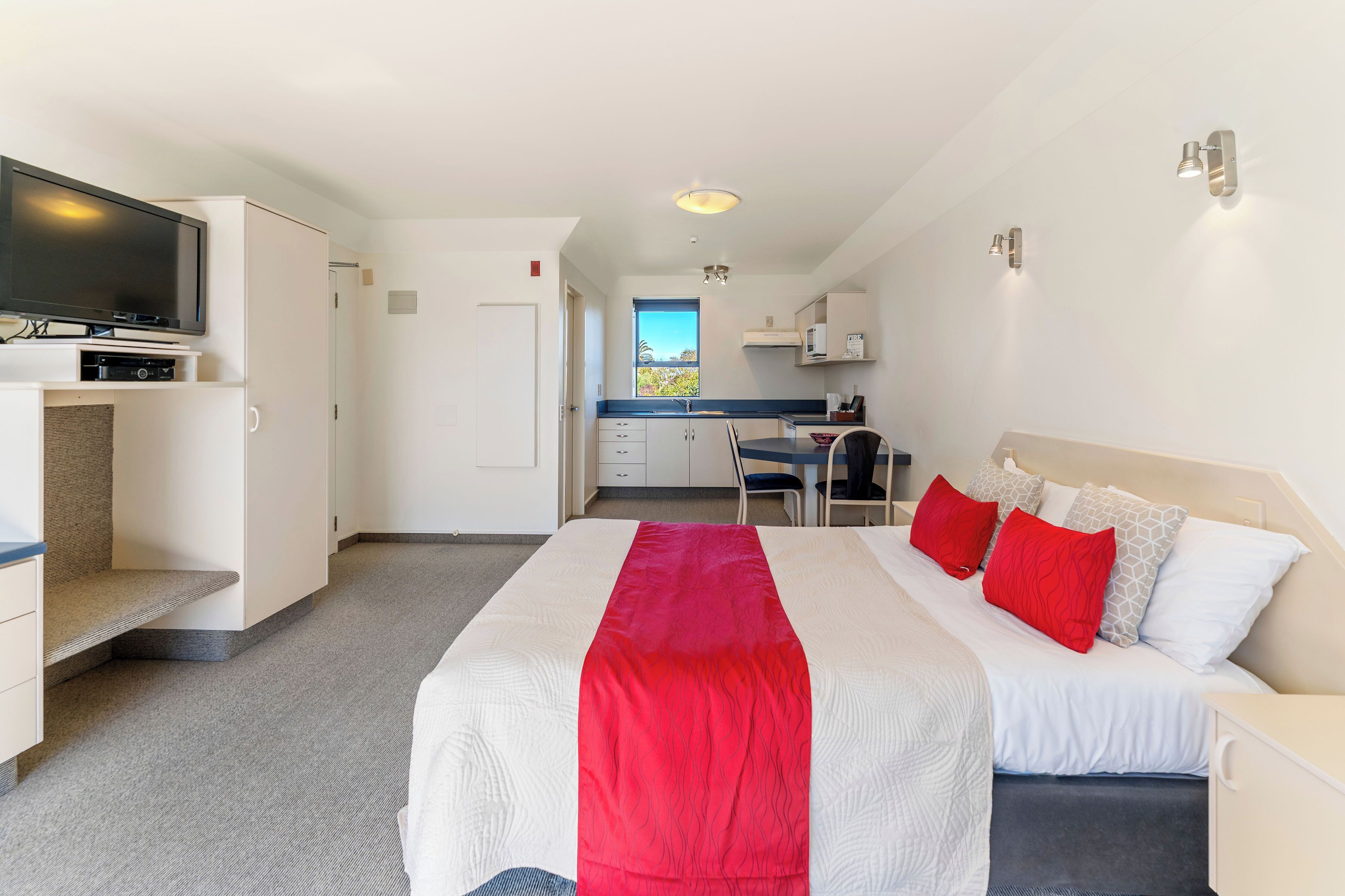 Ein Hotelzimmer mit Bett, Fernseher, Schreibtisch und Küchenzeile.