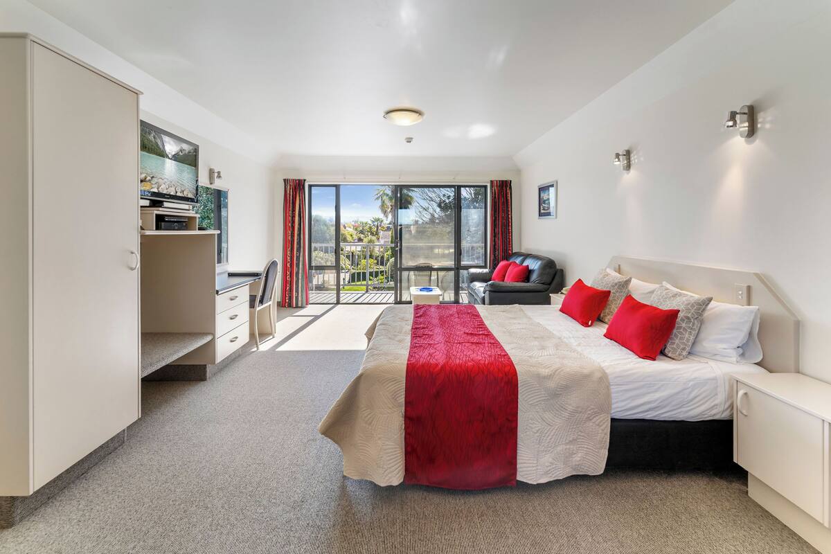A hotel room with a large bed, a desk, a chair, and a view of the outdoors.