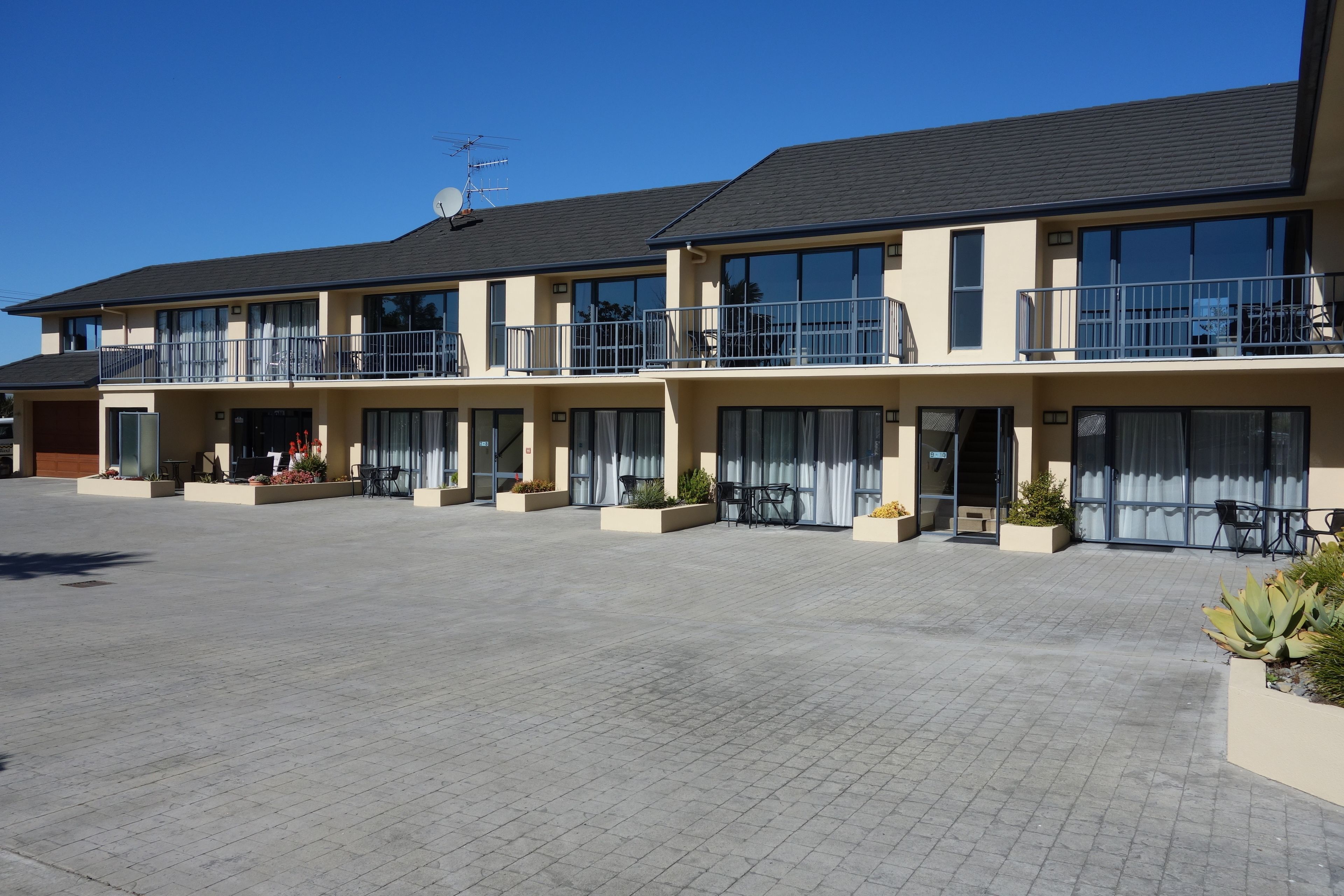 A multi-story hotel with balconies, large windows, and a paved courtyard.