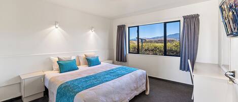 A hotel room with a large bed, a desk, a window with a view of the mountains, and a flat-screen TV mounted on the wall.