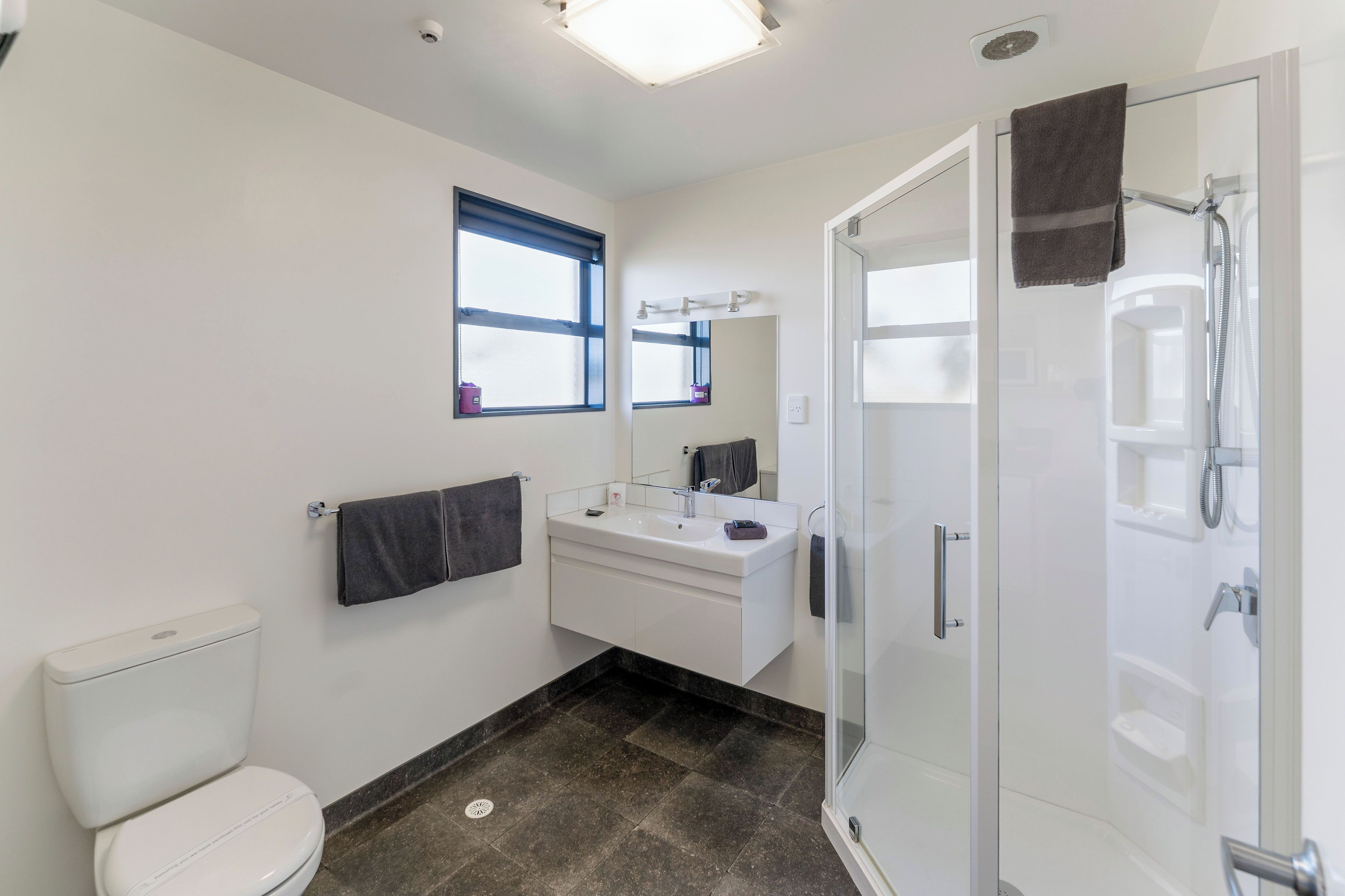 Een moderne badkamer met toilet, wastafel, spiegel en douchecabine.