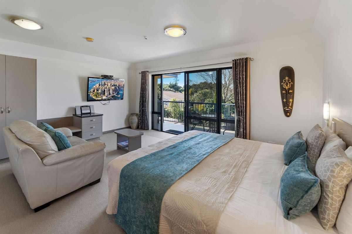 A modern hotel room with a large bed, a sofa, a desk, and a TV.