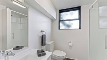A modern bathroom with a white sink, a mirror, a toilet, and a shower.