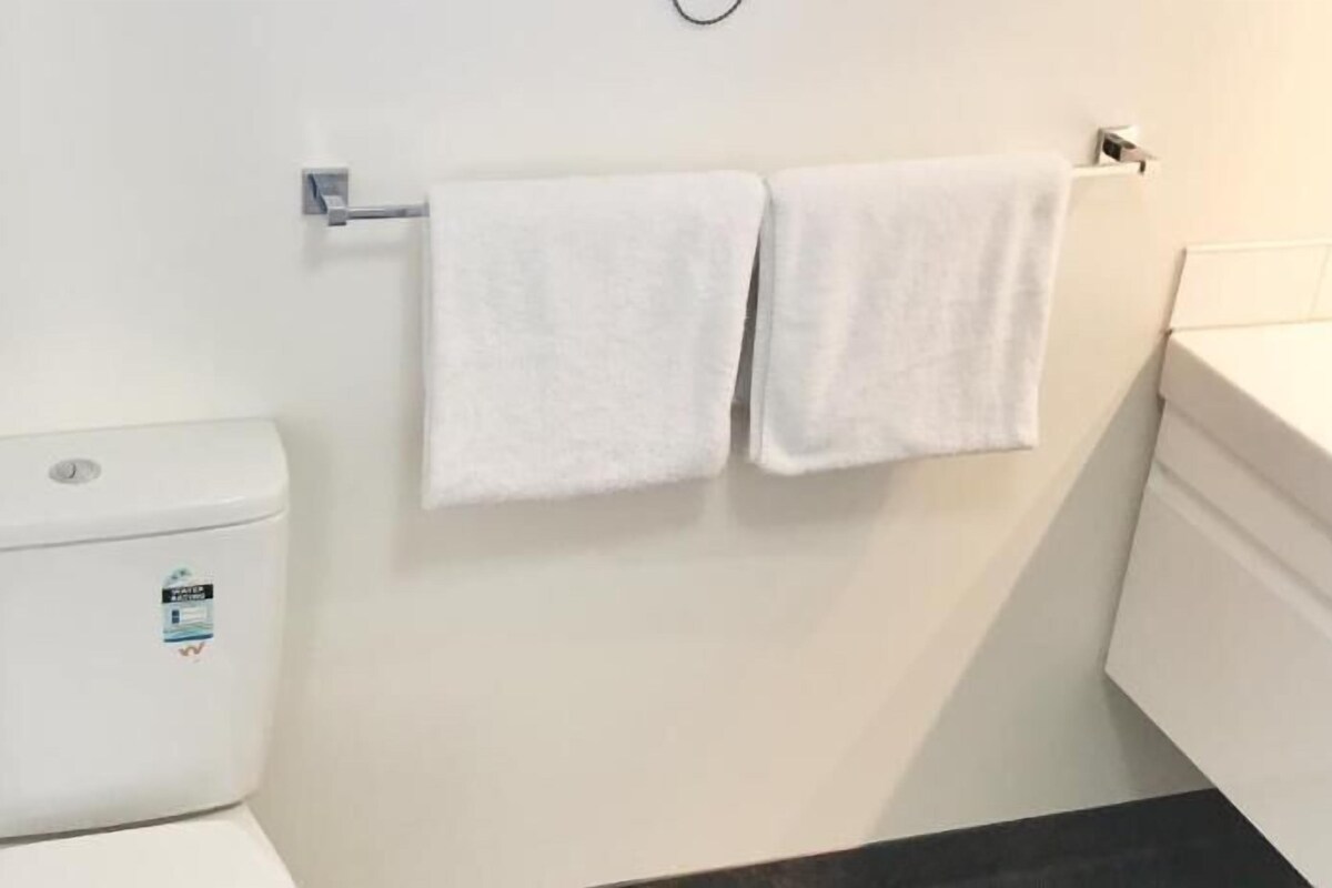 Een badkamer met een toilet, een handdoekhouder met twee handdoeken en een witte wasbak.