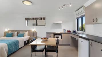A compact hotel room with a bed, bedside table, and a small kitchenette.