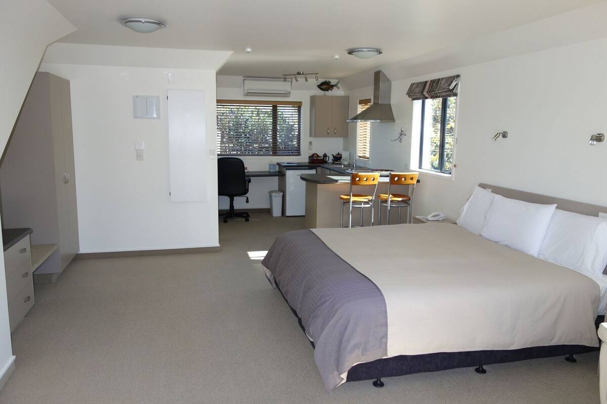 A bedroom with a bed, a desk, and a kitchenette.