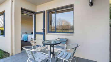 A balcony with a table and chairs, a bed in the background, and a view of trees and buildings.