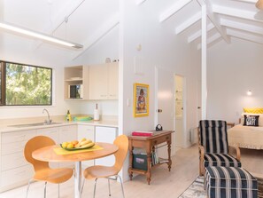 A modern kitchen with a dining area, a small table with chairs, and a bookshelf. - Craicor Accommodation (Paihia)