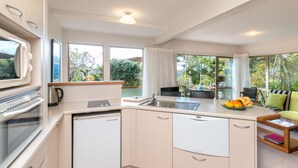 A modern kitchen with a built-in oven, a coffee maker, and a dishwasher. There is a dining area with a table and chairs, and a view of the outdoors through large windows.