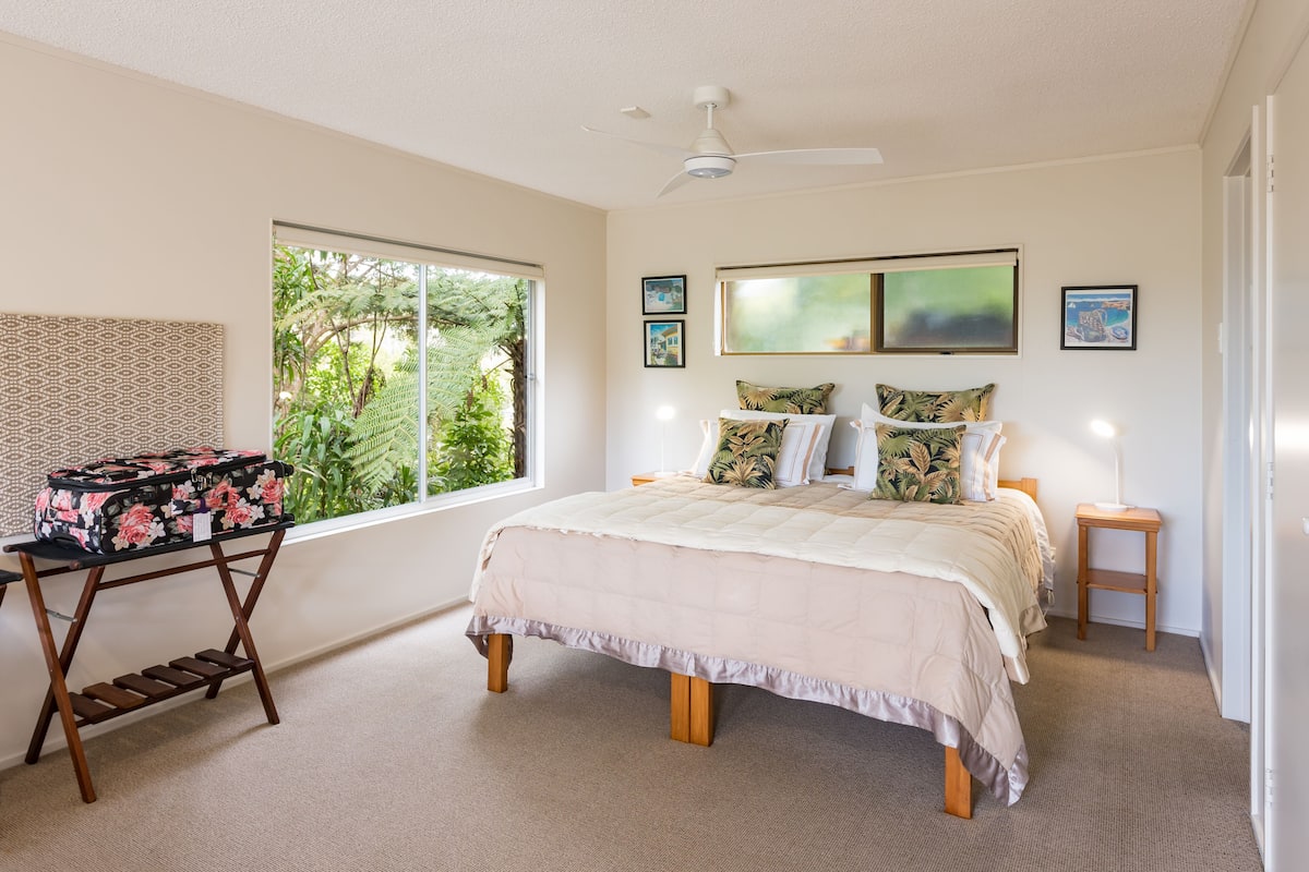 A bedroom with a bed, a standing lamp, a small table, and a suitcase on a stand.