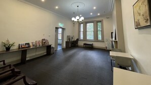 A spacious room with a high ceiling, recessed lighting, a chandelier, a long reception desk, and a bench. - The George Sydney - Hostel (Haymarket)