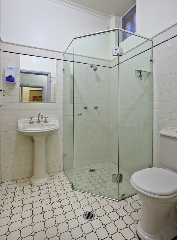 Un baño con cabina de ducha de vidrio, lavamanos pedestal y retrete.