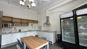 A modern kitchen with white cabinetry, a wooden dining table, and a black refrigerator. - The George Sydney - Hostel (Haymarket)