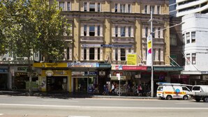 A historic building with multiple ground-floor shops, including a supermarket and a budget store. - The George Sydney - Hostel (Haymarket)