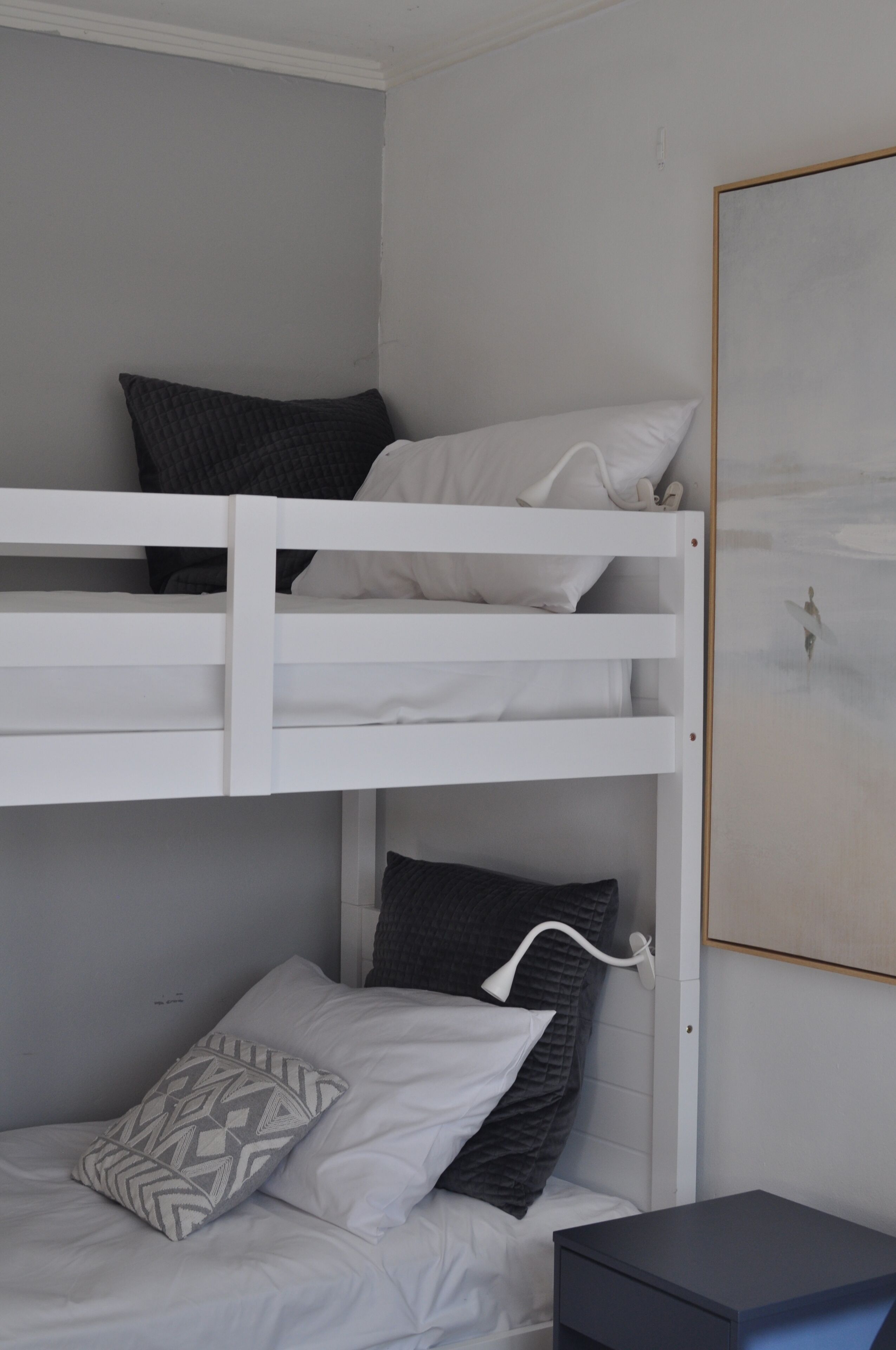 Un lit superposé avec une literie blanche, un oreiller gris et une petite table de chevet.