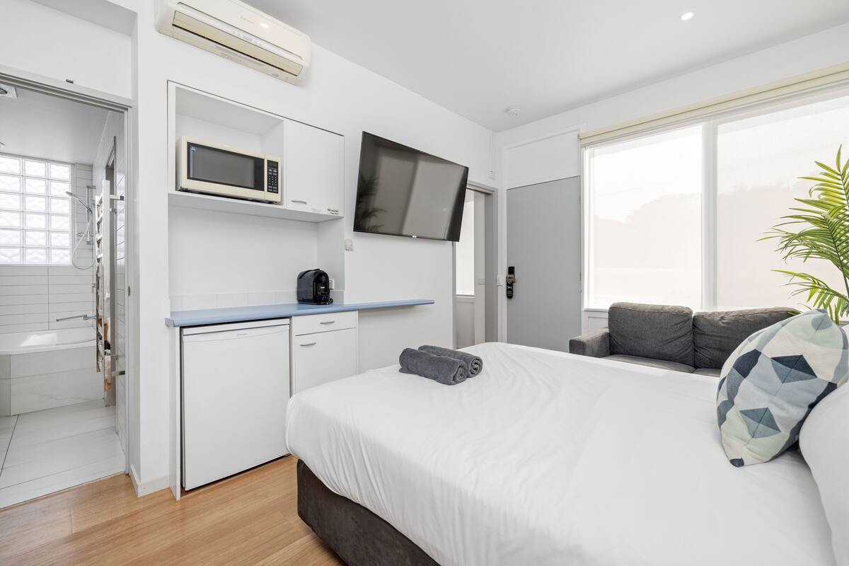 Quarto de hotel moderno com cama, televisão de tela plana, micro-ondas e uma pequena cozinha equipada.