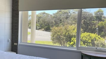A hotel room with a bed, a window with a view of trees and a road, and a small table.