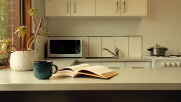 A kitchen with cabinets, a microwave, a stove, a coffee cup, and an open book.