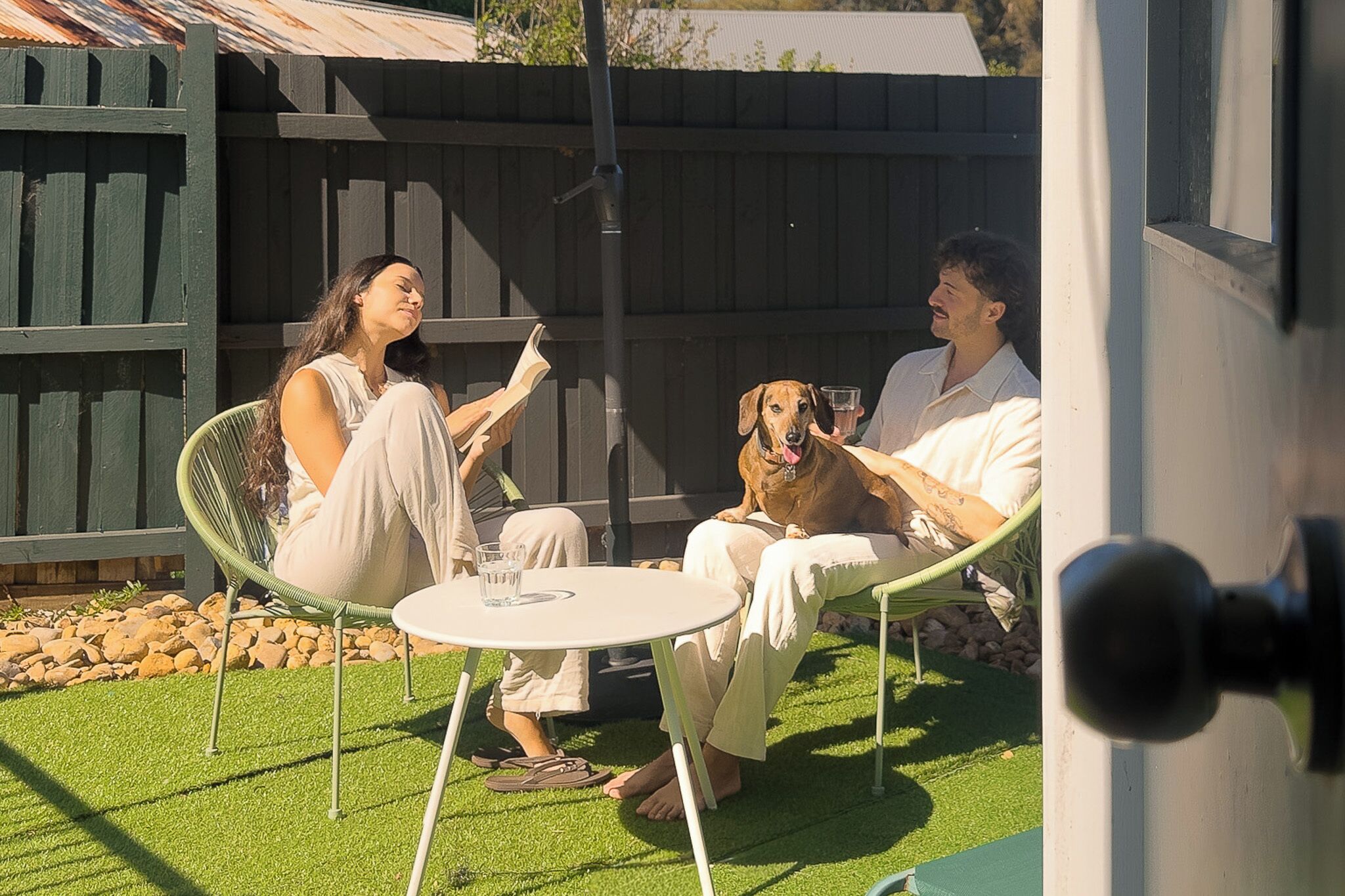 Un patio con una mesa redonda y sillas, una cerca de madera y un perro.