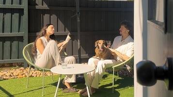 Un patio con una mesa redonda y sillas, una cerca de madera y un perro.