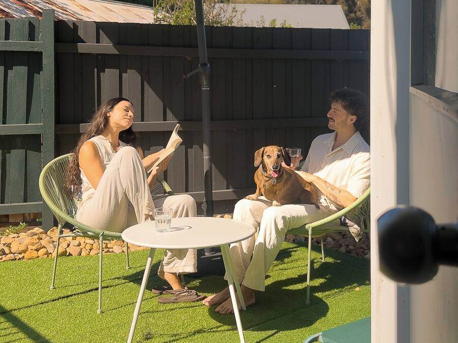 Un patio con una mesa redonda y sillas, una cerca de madera y un perro.