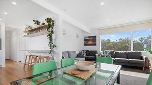 A modern living room with a glass dining table, green chairs, and a grey sofa. - Moody's Motel (Blairgowrie)