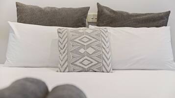 A bed with white and patterned pillows, a white mattress, and gray pillows at the foot of the bed.