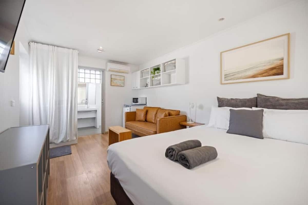 Quarto de hotel com cama, sofá, escrivaninha e televisão.