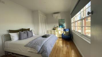 A bedroom with a bed, a chair, a window, and a bedside table.